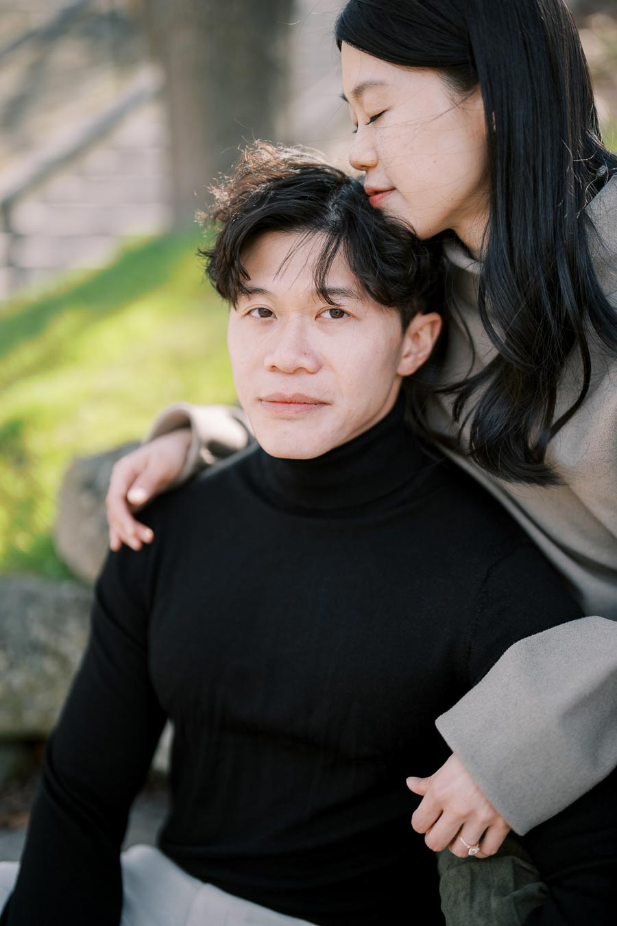 A tender moment captured between a couple sitting outdoors, with the woman gently resting her head on the man's shoulder.