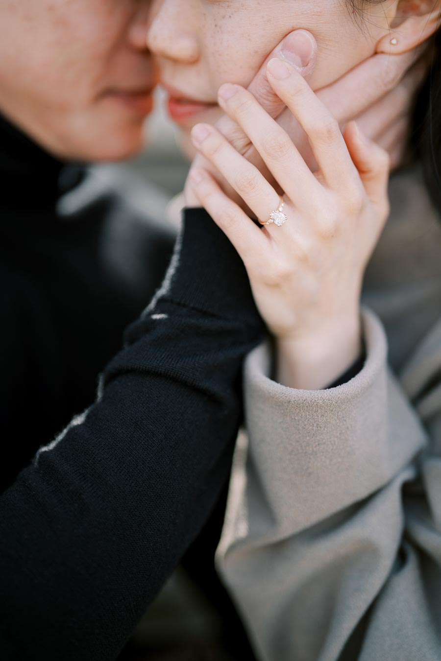 A close-up shot of a couple embracing, highlighting a woman's hand adorned with an engagement ring.