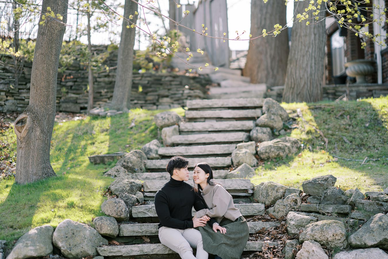 A couple enjoys a peaceful moment sitting on stone steps in a lush, green park setting.
