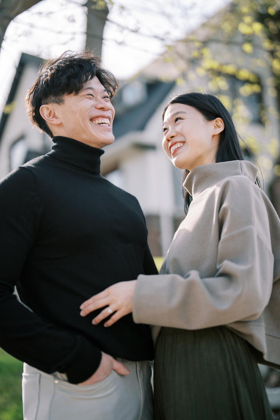 A happy couple shares a moment outdoors, smiling at each other with a house in the background.