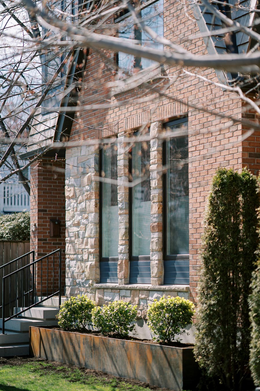 A close-up view of a house facade featuring a combination of brick and stone, with large windows and a small garden in front.