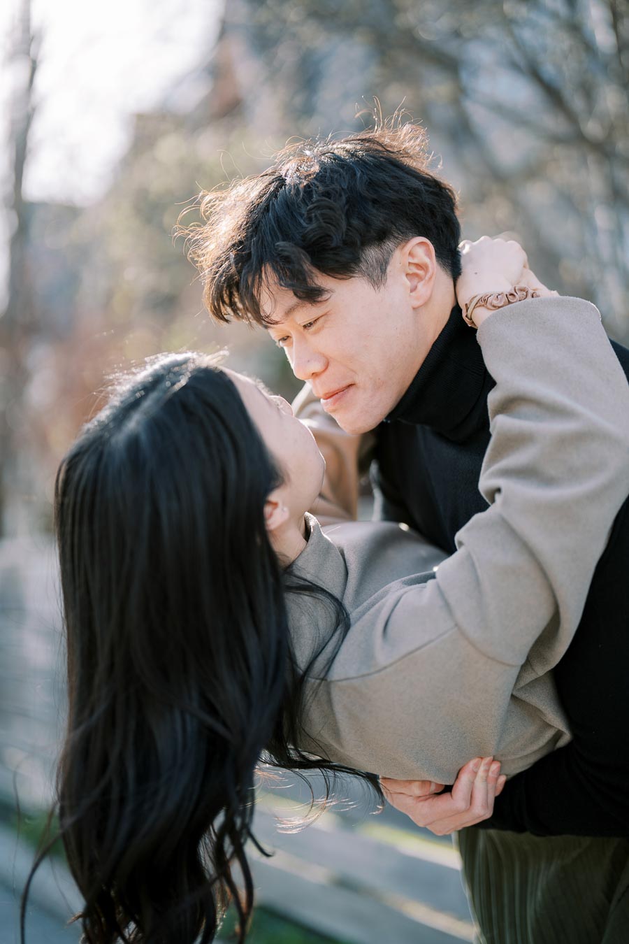 A couple shares a tender moment outdoors, with the man holding the woman in a dip as they gaze into each other's eyes.