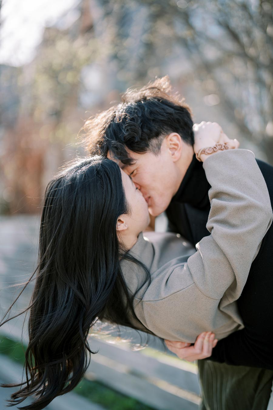 A couple shares a romantic kiss outdoors, surrounded by a softly blurred background, suggesting a serene and intimate moment.