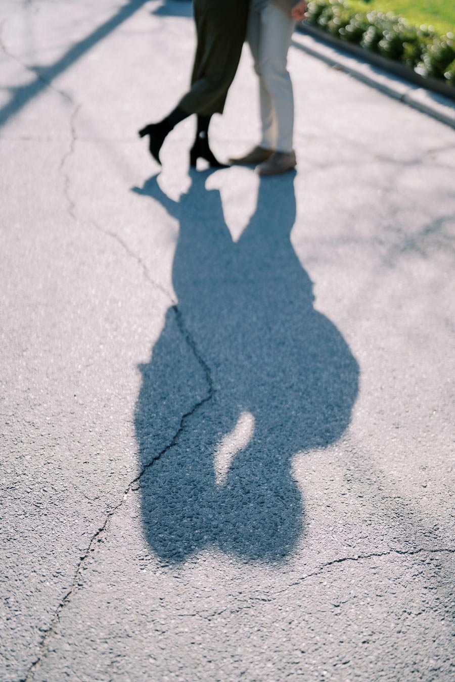 The shadow of a couple sharing a kiss is cast on a sunlit paved street, capturing a romantic moment.