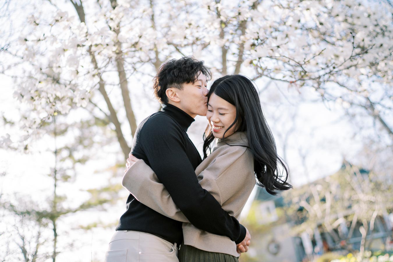 A couple shares a tender moment under cherry blossoms, symbolizing love and springtime.