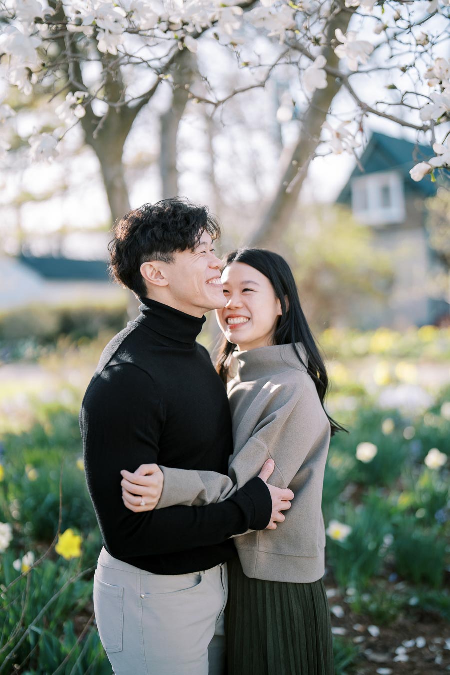 A couple embraces under a blooming tree, surrounded by spring flowers in a garden.