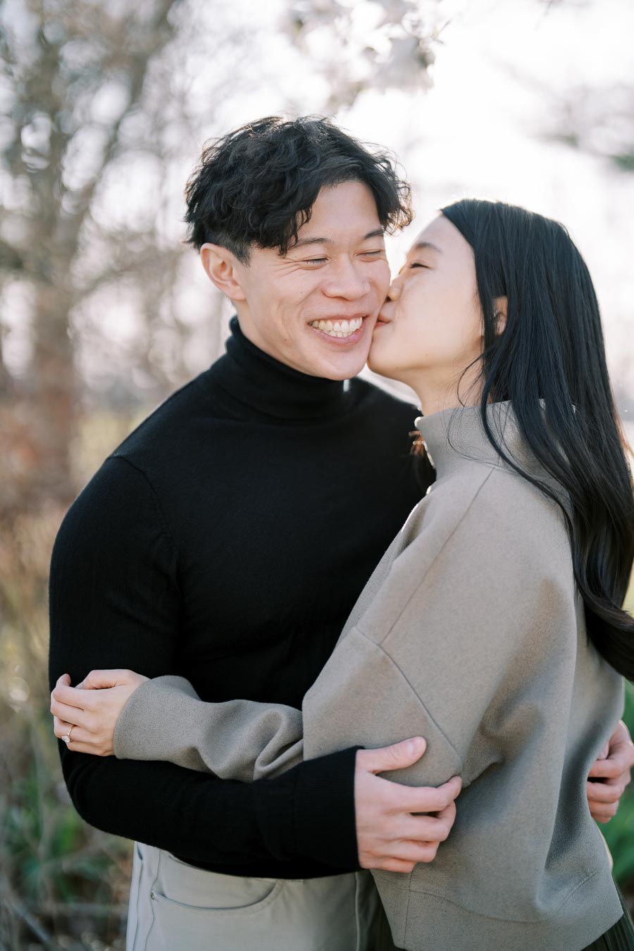 A joyful couple shares a tender moment outdoors, with the woman giving the man a kiss on the cheek.