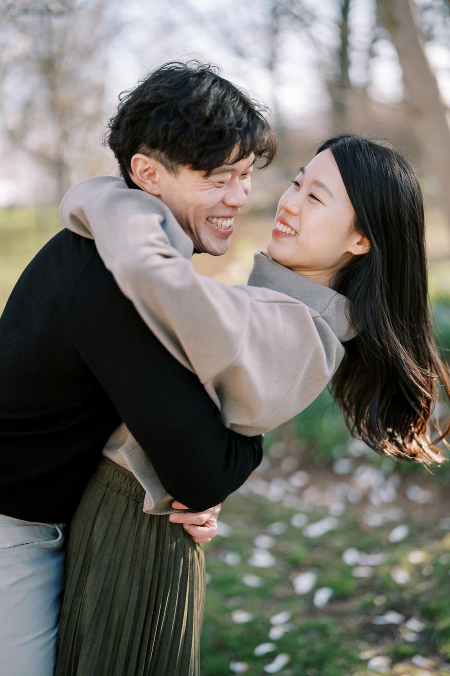 A joyful couple shares a warm embrace in a park, surrounded by trees and greenery.