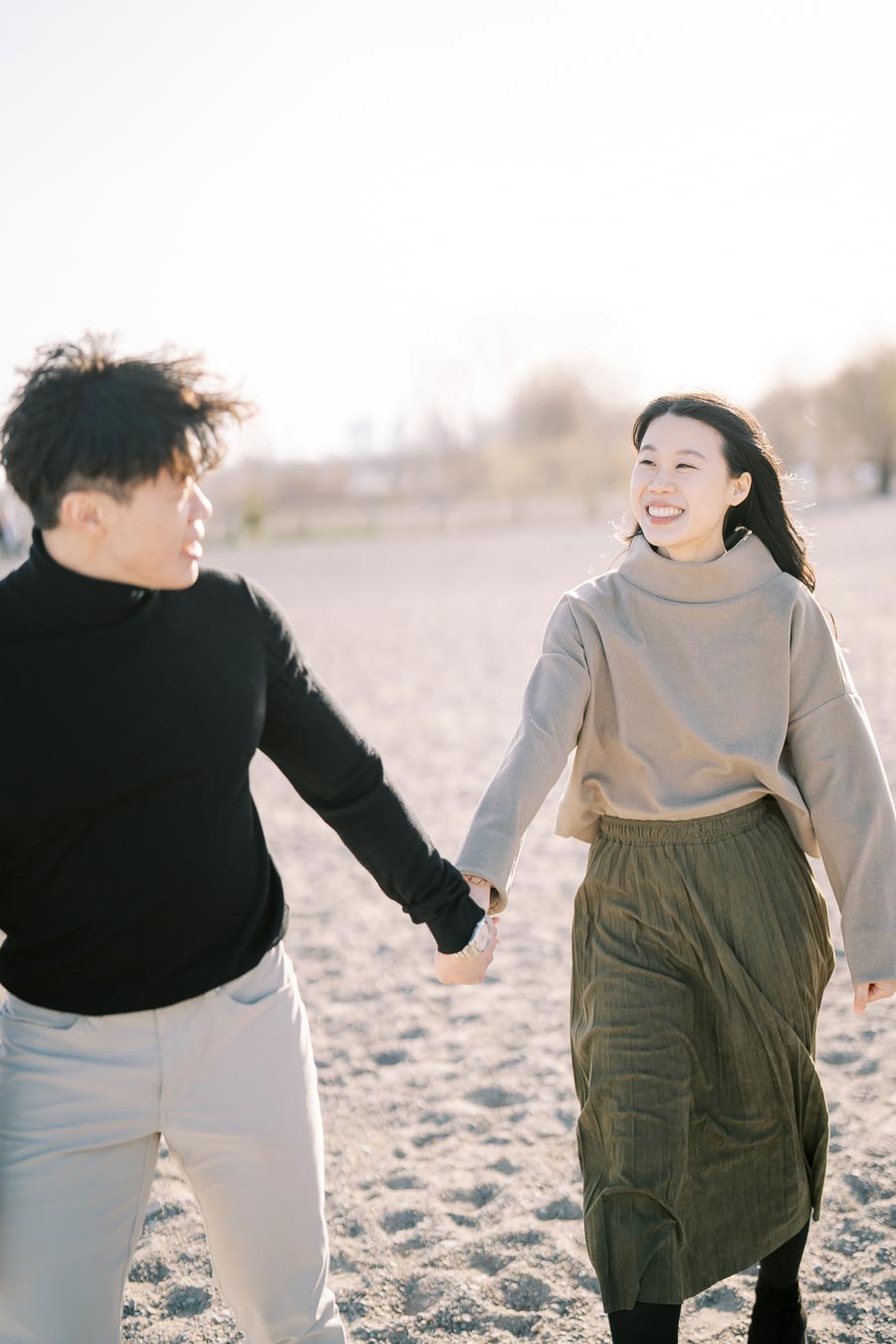 A couple joyfully walking hand in hand on a sandy beach.