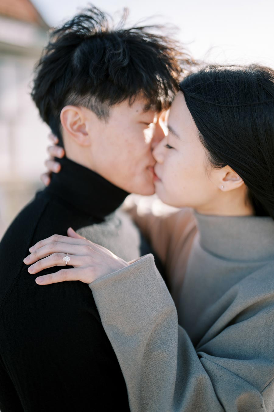 A couple shares a tender kiss, with the woman displaying a ring on her left hand.