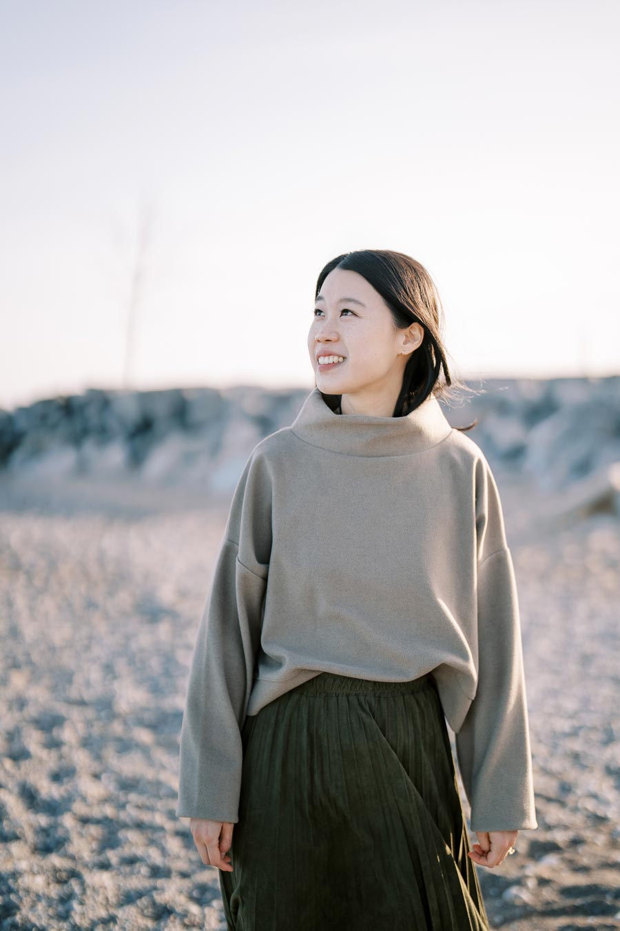 A woman enjoys a serene moment on the beach, dressed in a cozy gray sweater and a green skirt.