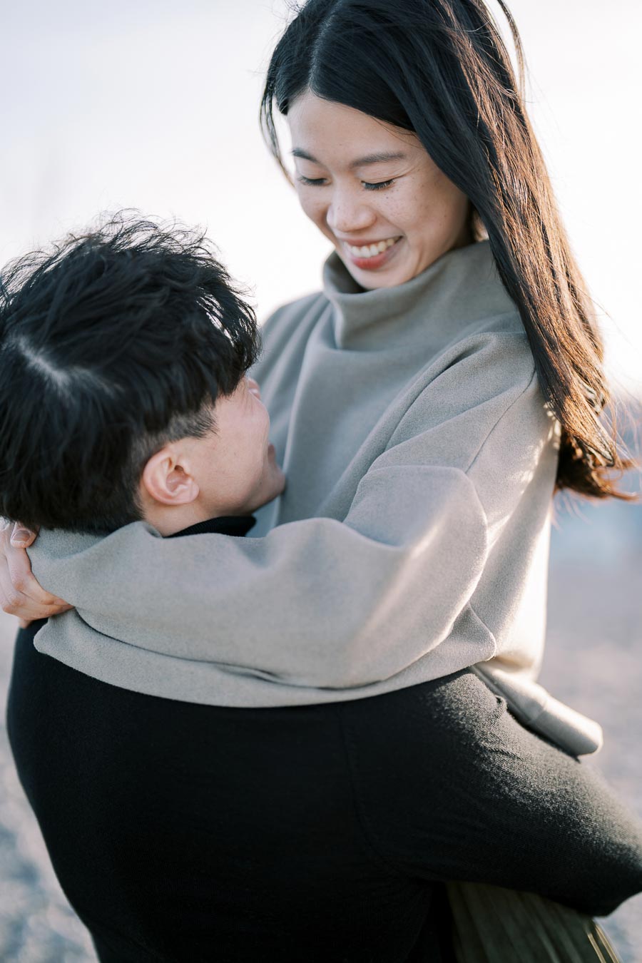 A joyful couple shares a warm embrace, smiling at each other in an outdoor setting.