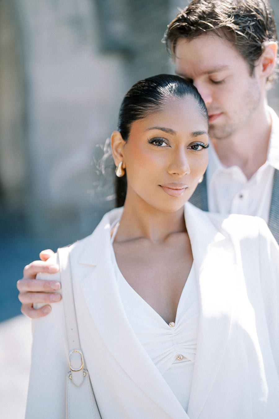 A couple posing for an engagement portrait, with the woman in a white outfit and the man in a light-colored suit.