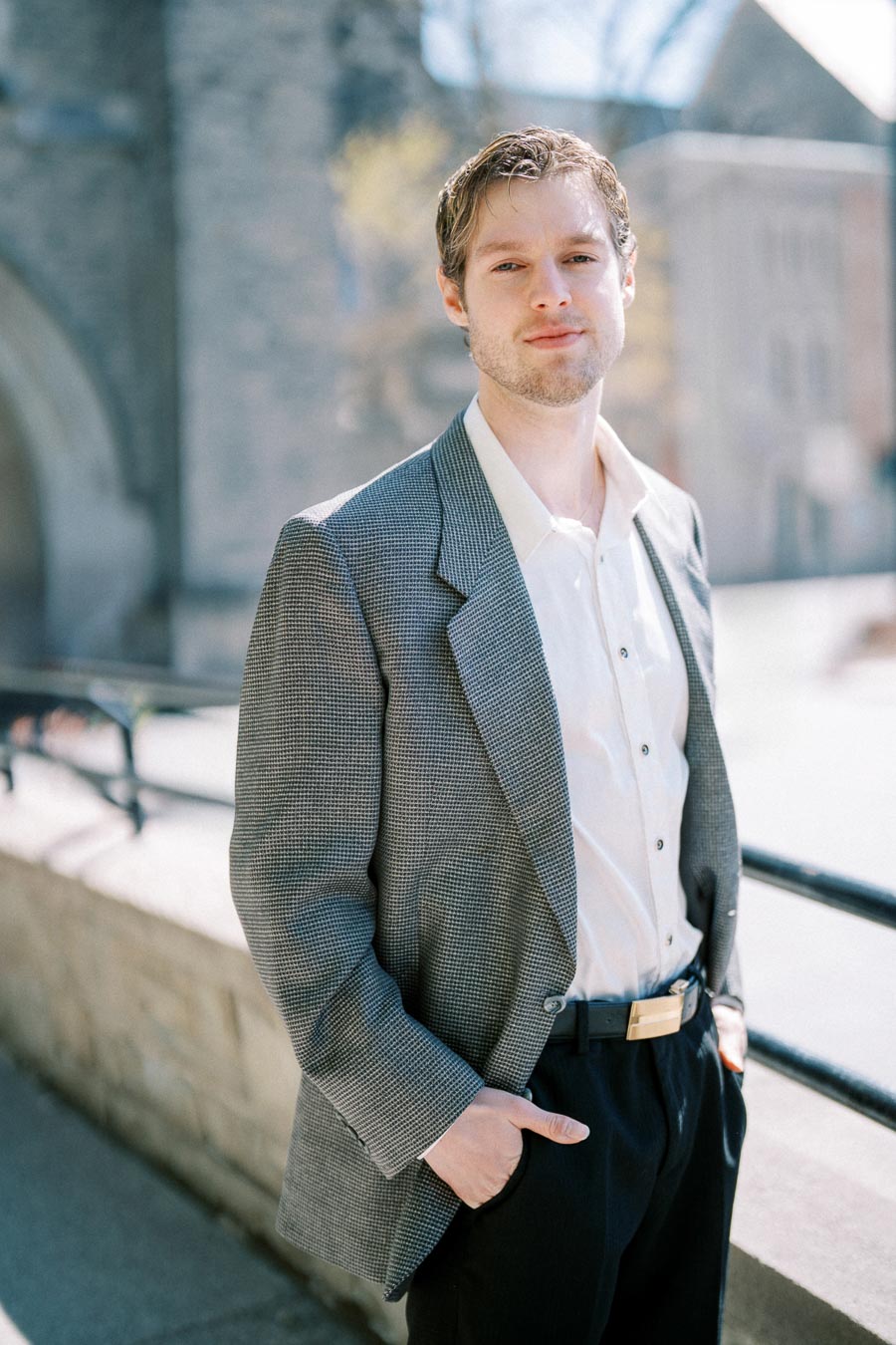 Man wearing a gray blazer over a white shirt, standing outdoors with a neutral expression.