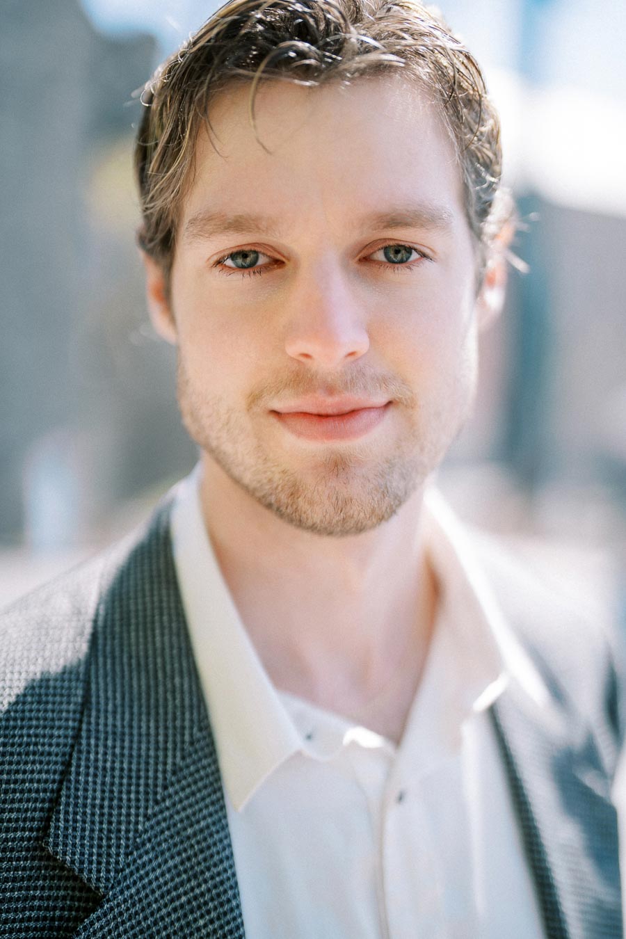 Close-up portrait of a young man with light brown hair wearing a suit and a white shirt.