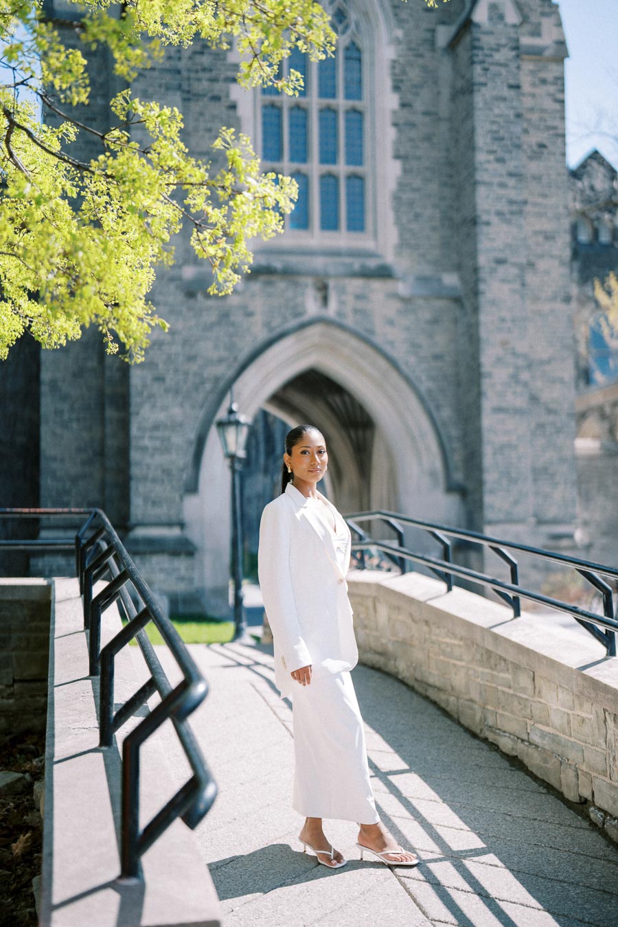 Woman wearing a white outfit standing on a stone pathway at the University of Toronto.