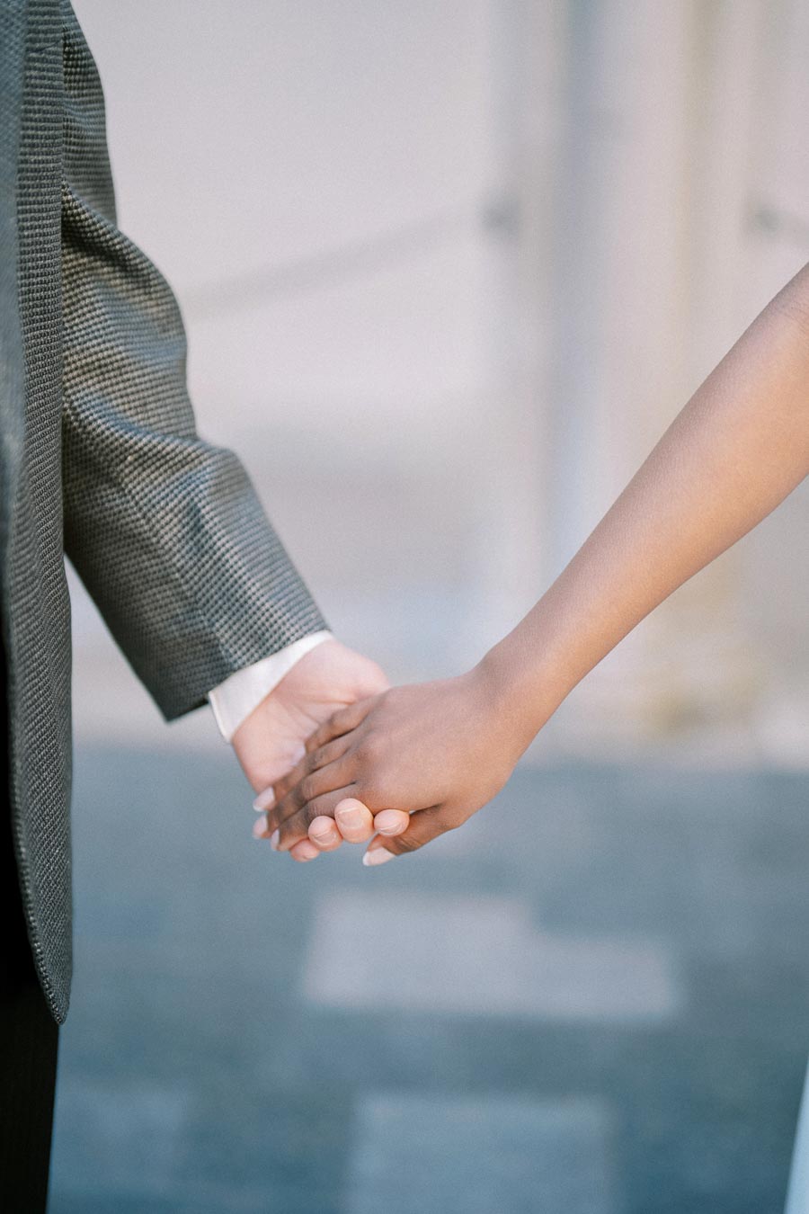 A close-up of two people holding hands, one in a suit jacket and the other with a bare arm, symbolizing connection and support.