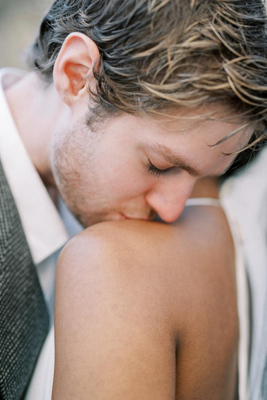 A close-up of a man gently kissing a woman's shoulder, conveying intimacy and affection, captured in soft, natural lighting.