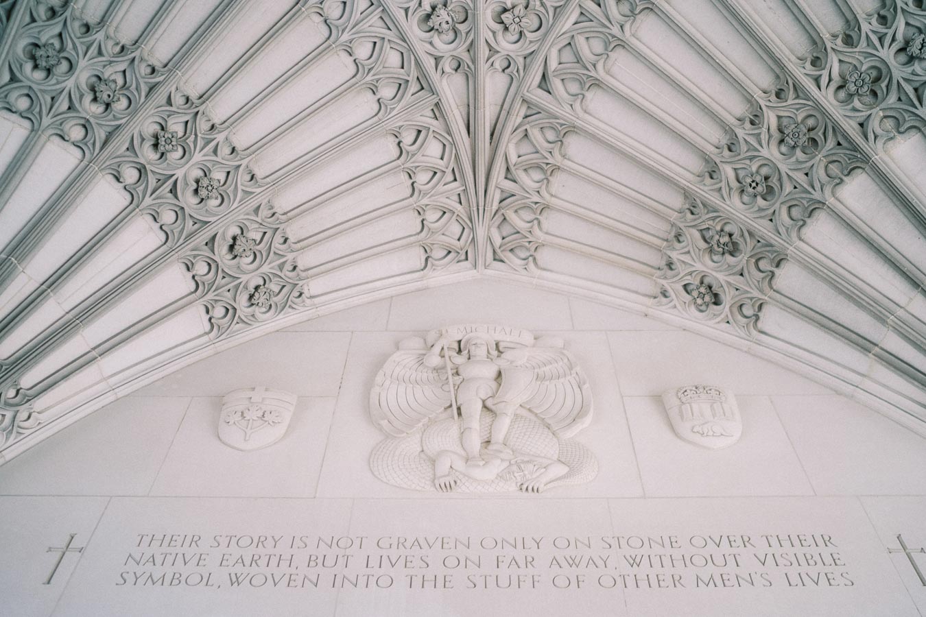 Engraved stone artwork featuring a central figure and text on a wall with intricate architectural details above.