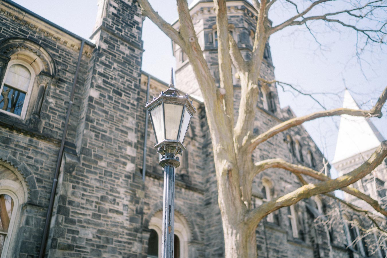 Historic building with a vintage street lamp and bare tree branches, under a clear blue sky.