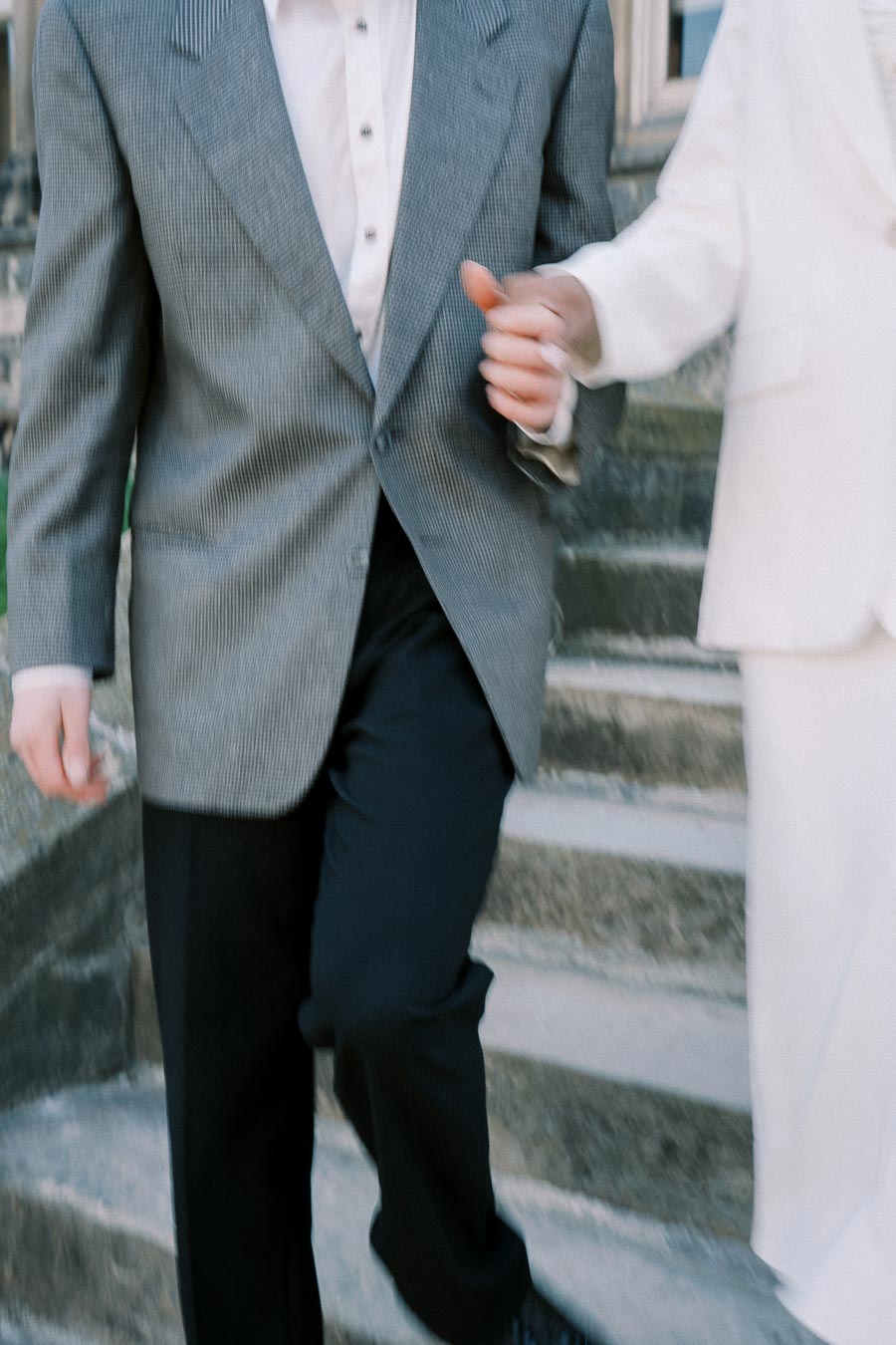 Two people in suits walking down stone steps, holding hands.