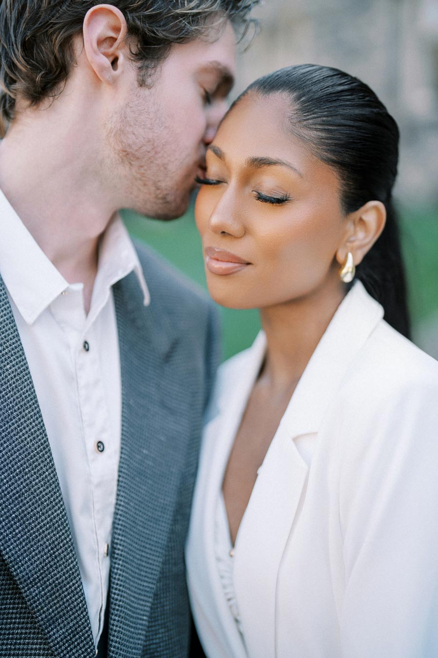 Couple sharing a tender moment, man kisses woman's forehead, both dressed in formal attire.
