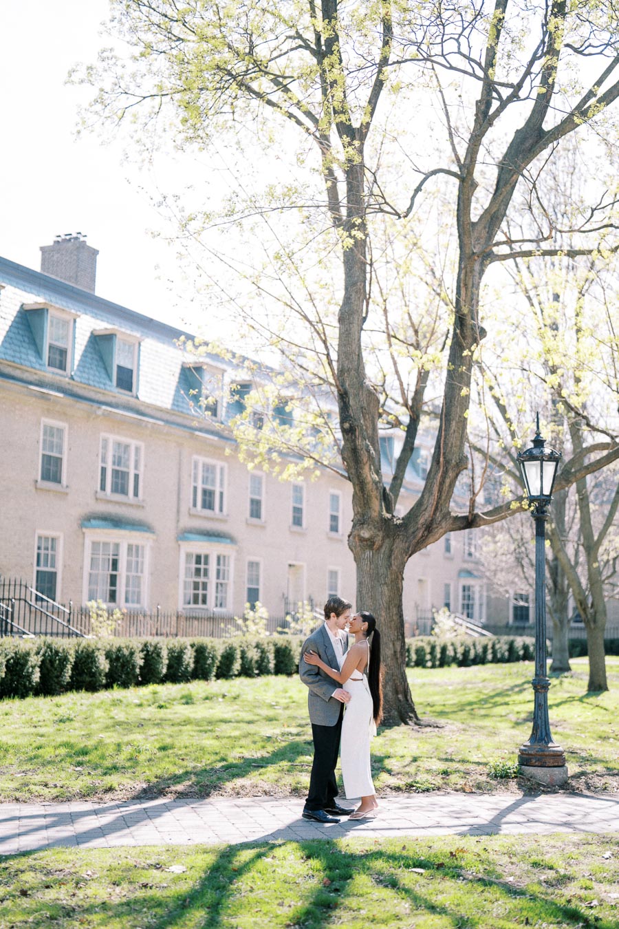 Couple standing under tree and sharing a quiet moment during spring engagement photoshoot at University of Toronto, Trinity College