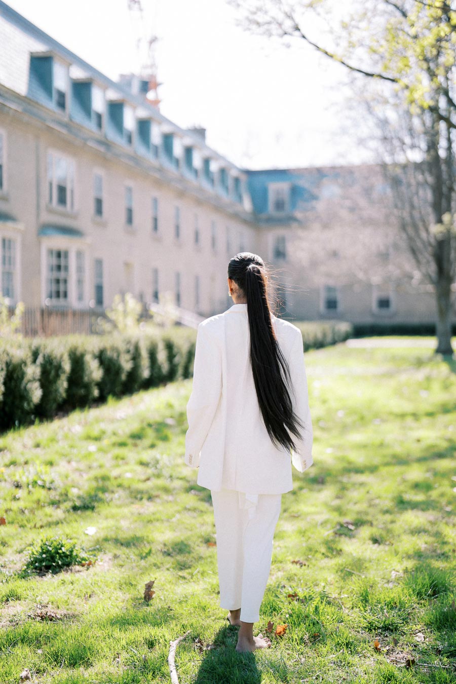 Woman in white walking barefoot on grass at Trinity College, University of Toronto during an engagement photoshoot