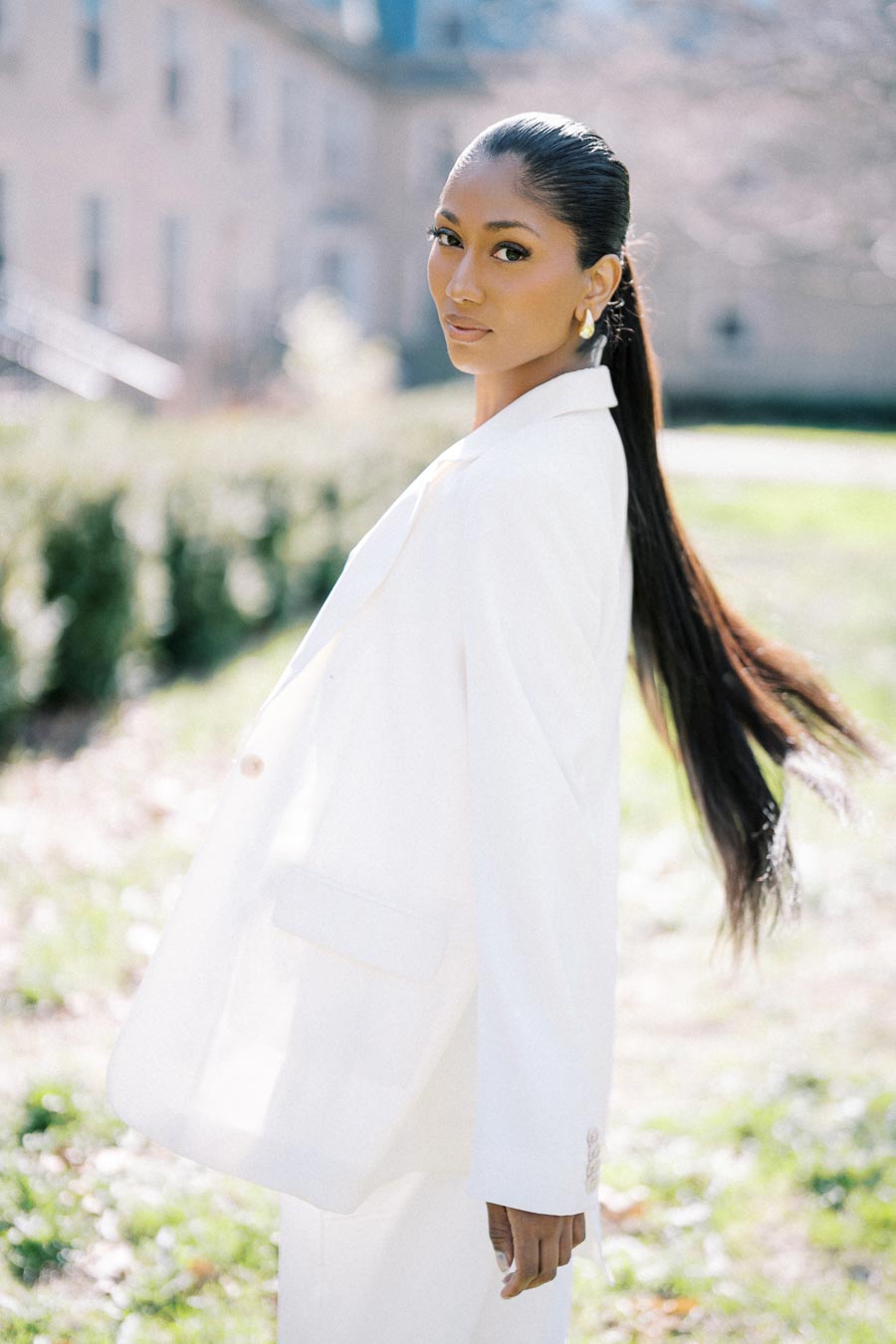 Stylish woman in a white suit posing confidently during engagement photoshoot at University of Toronto Trinity College