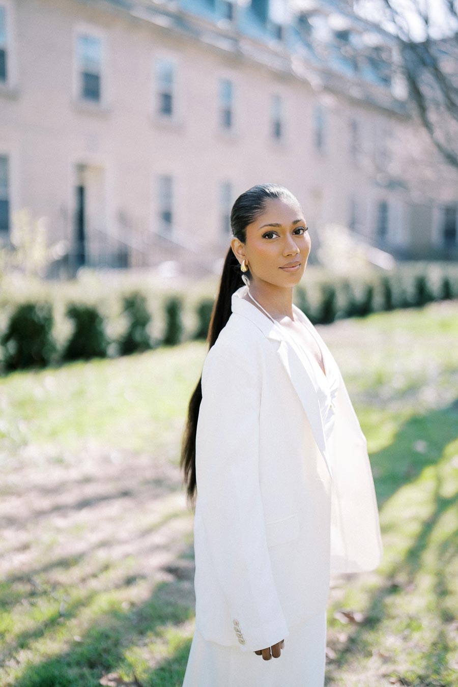 Confident woman in a white suit during an outdoor engagement photoshoot at Trinity College, University of Toronto