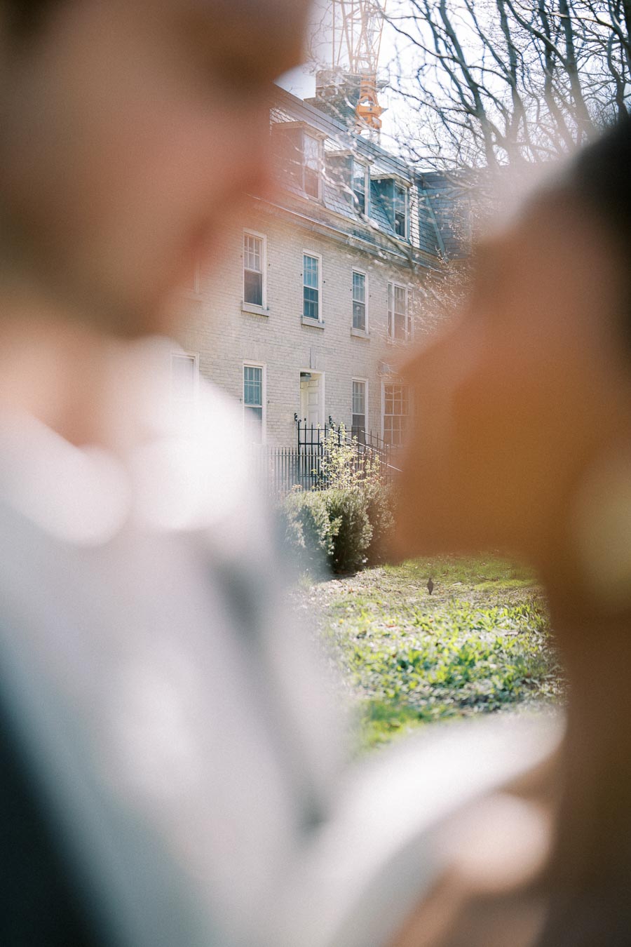 Creative blurred foreground of a couple framing a historic Toronto house during their engagement session