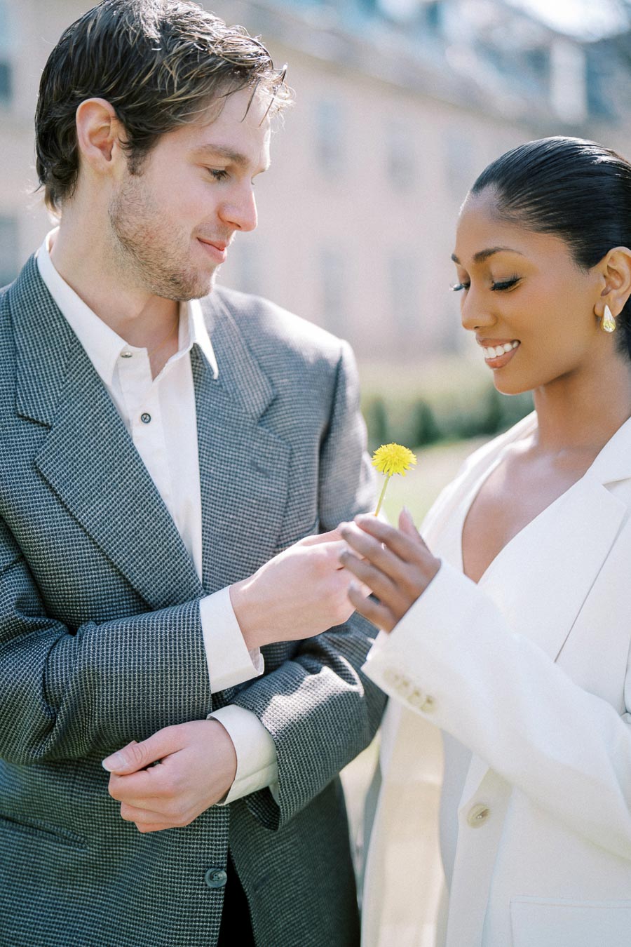 Close-up of a couple smiling and holding a dandelion during their spring engagement photoshoot in Toronto