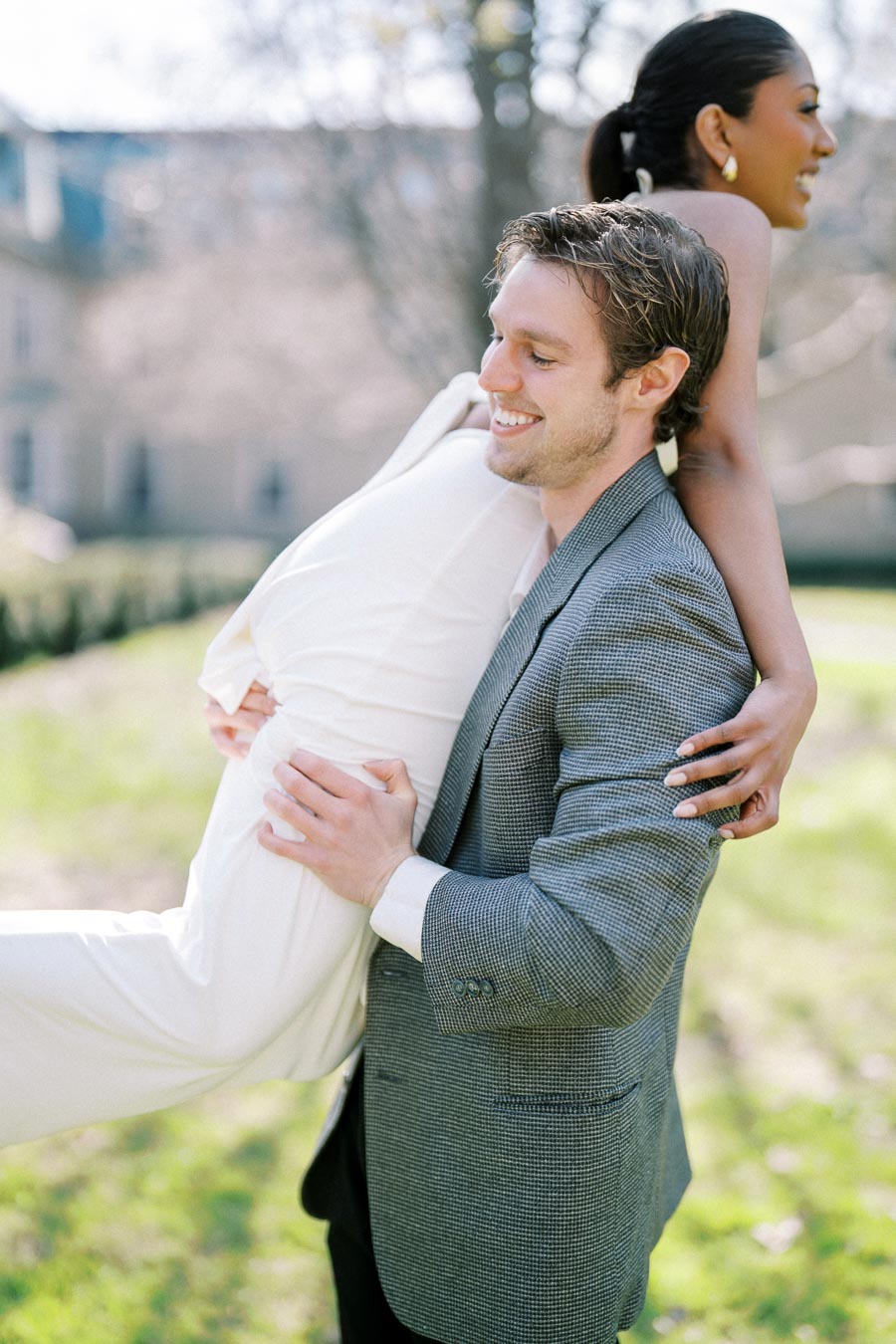 Joyful groom lifting bride-to-be during their sunny engagement session in a Toronto garden setting