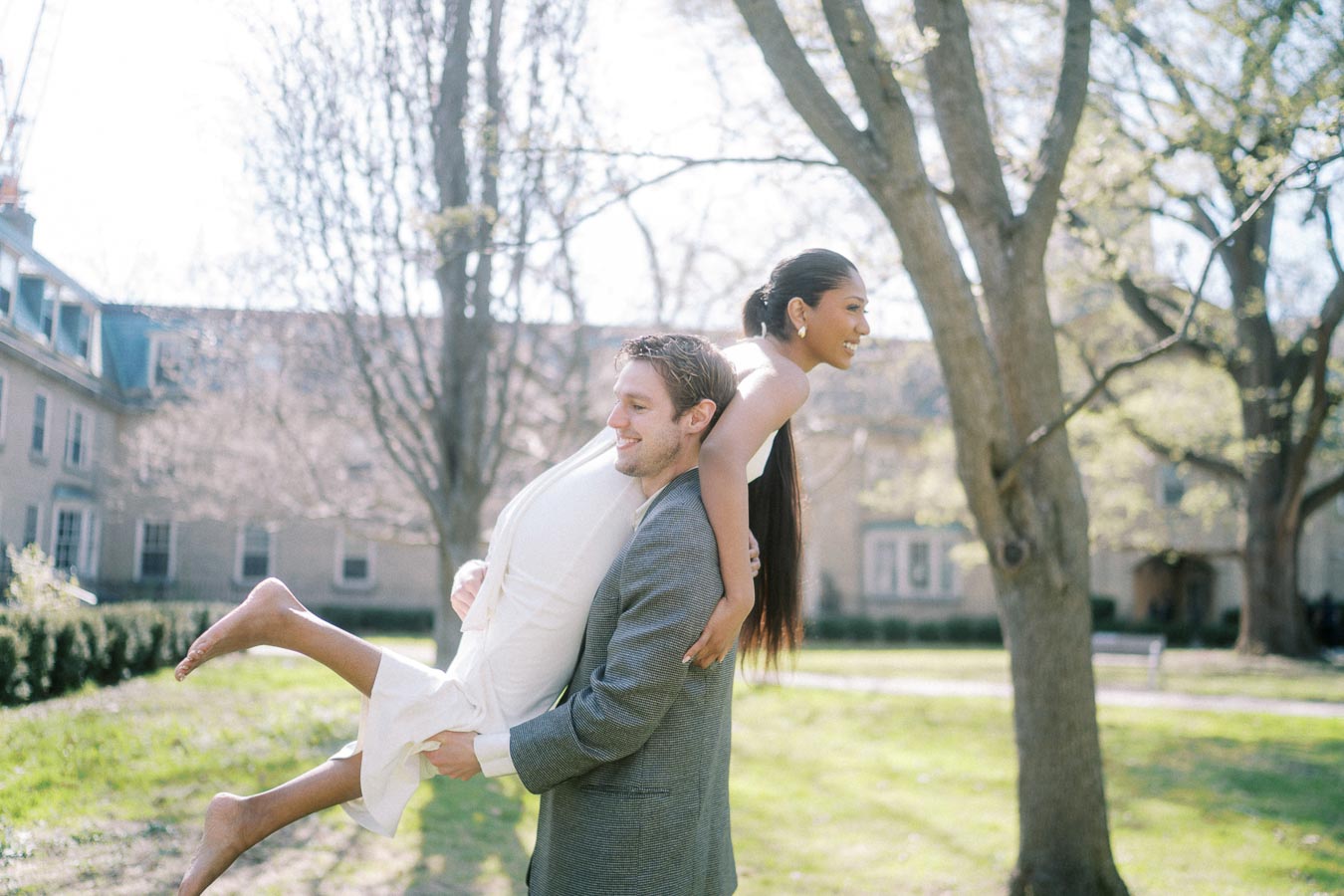 Groom-to-be lifting his barefoot fiancée during playful spring engagement shoot in Toronto park