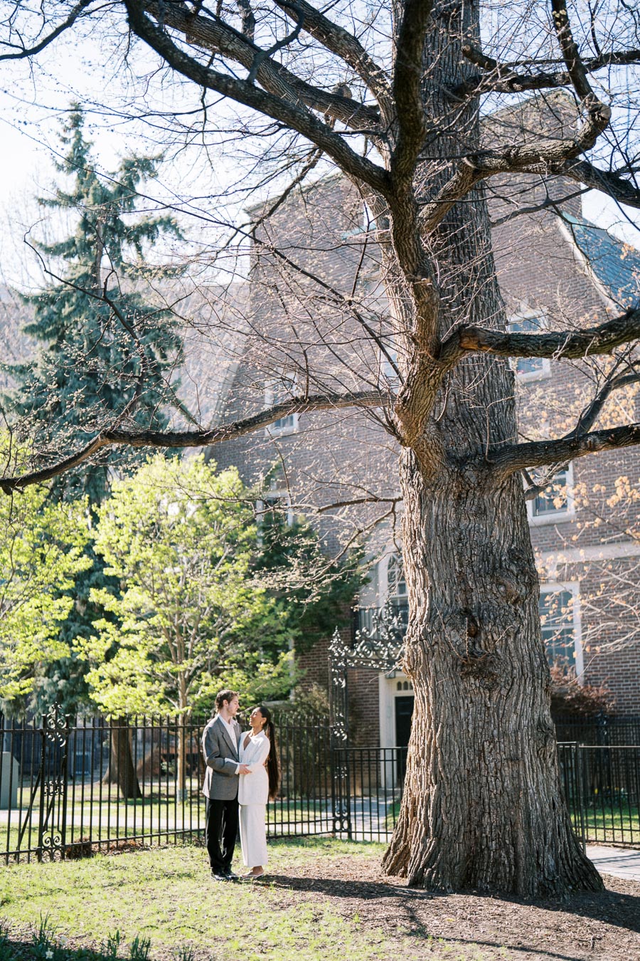 Couple standing under large tree during spring engagement session in Toronto