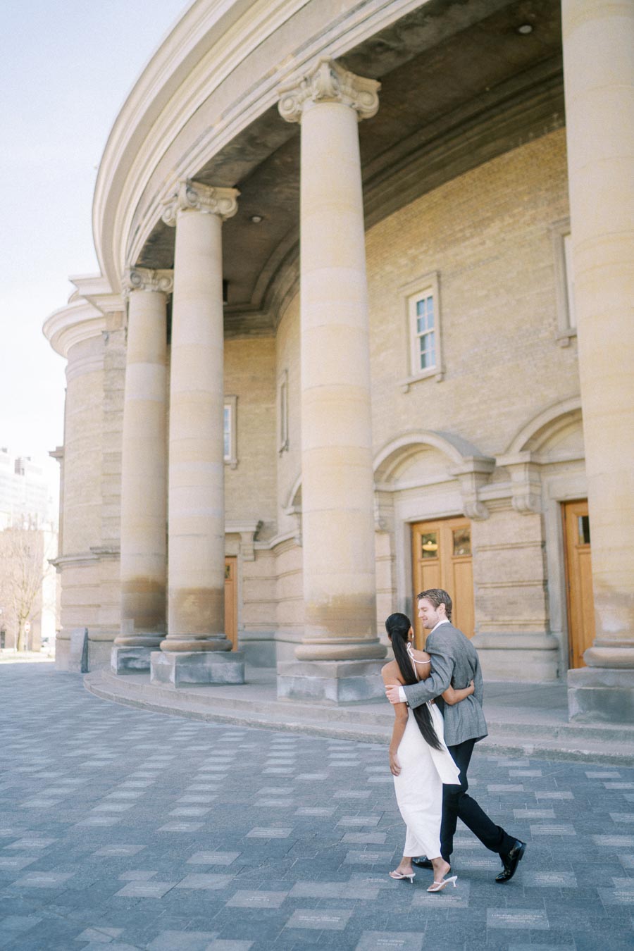 Engaged couple walking together in front of historic building with columns in Toronto
