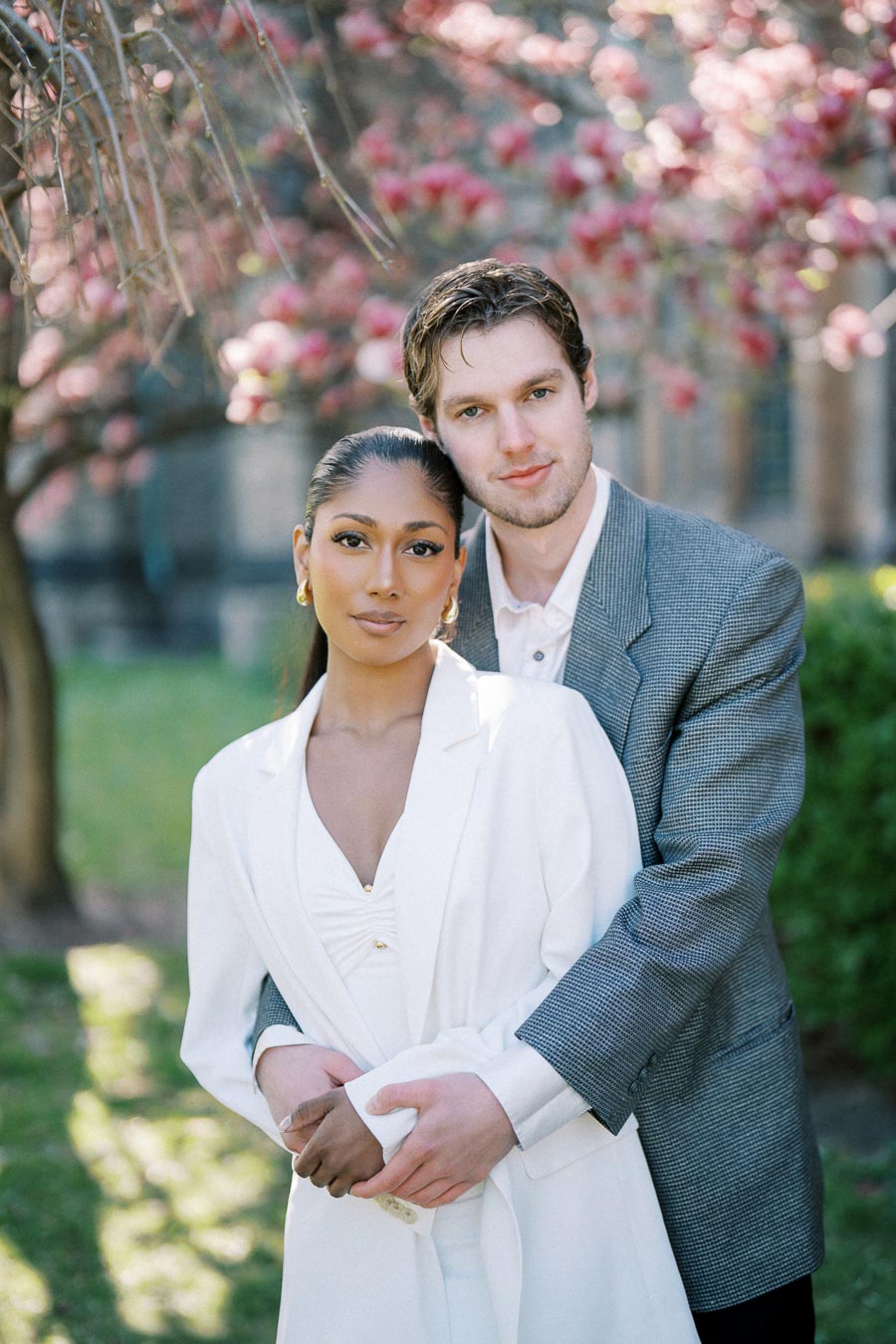 Engaged couple posing in spring sunlight under cherry blossoms at University of Toronto