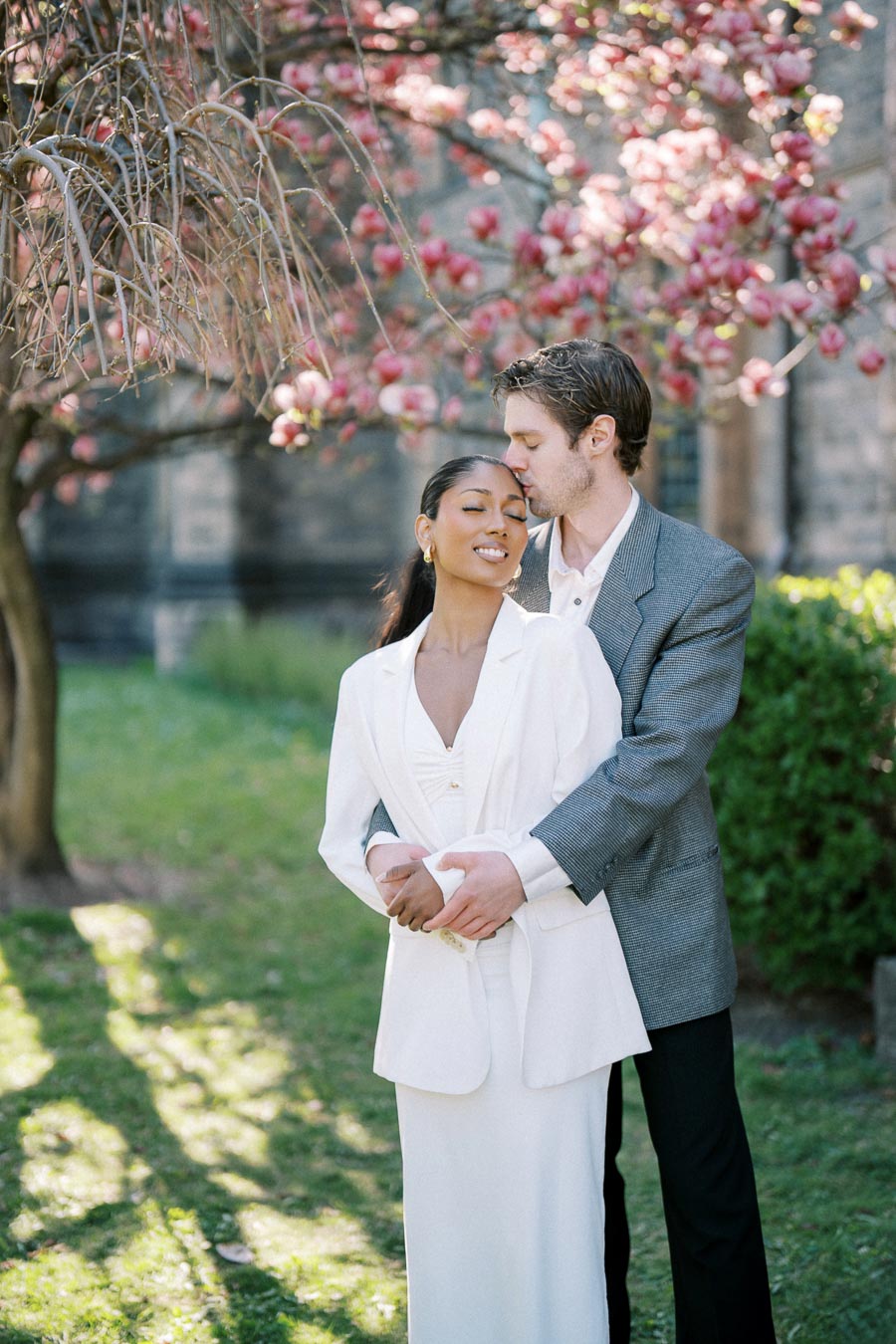Engaged couple sharing a kiss under magnolia blossoms at University of Toronto in spring