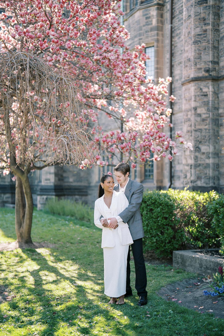 Engaged couple standing under blooming magnolia tree at University of Toronto during spring photoshoot