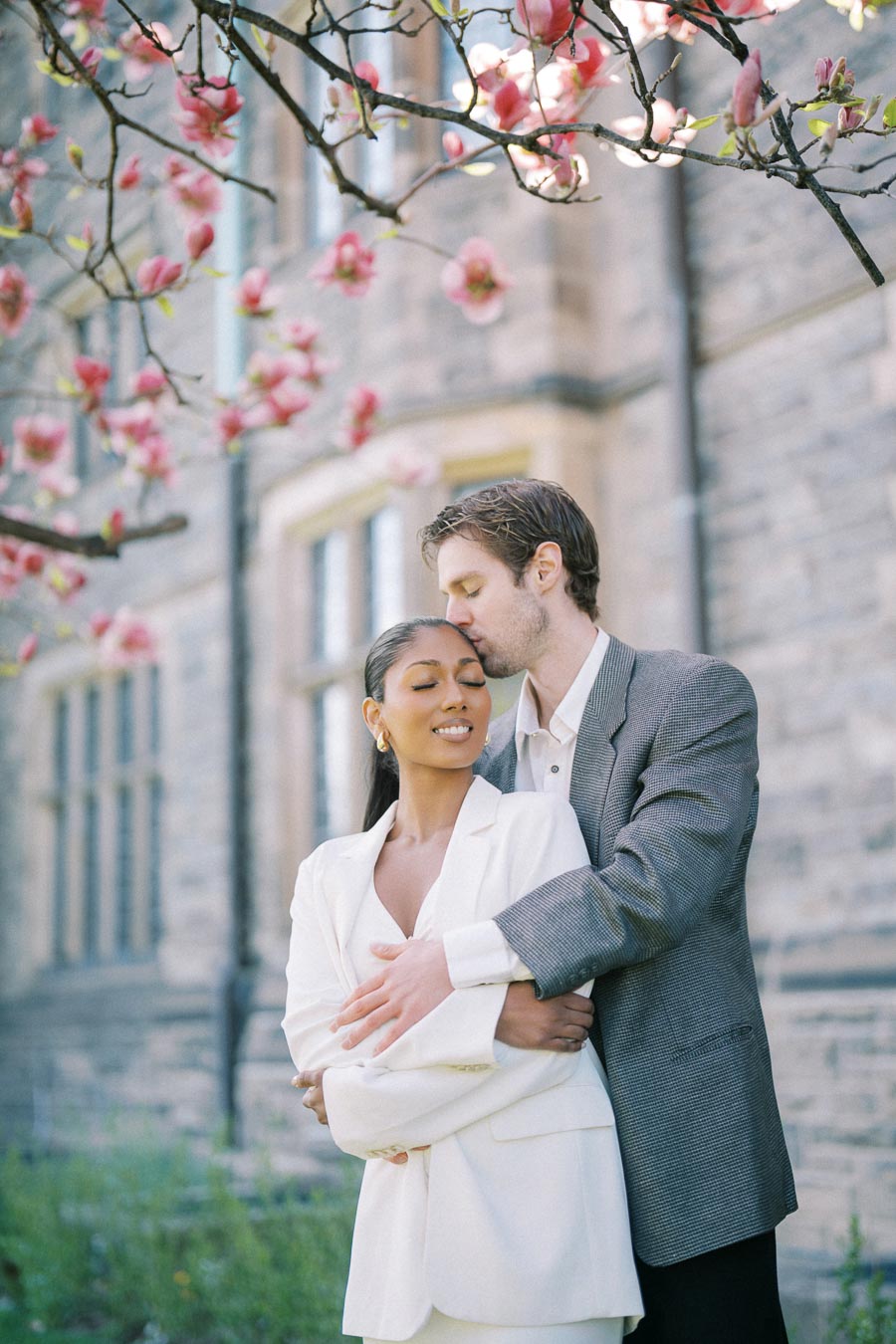 Engaged couple embracing under magnolia blossoms at Trinity College, University of Toronto