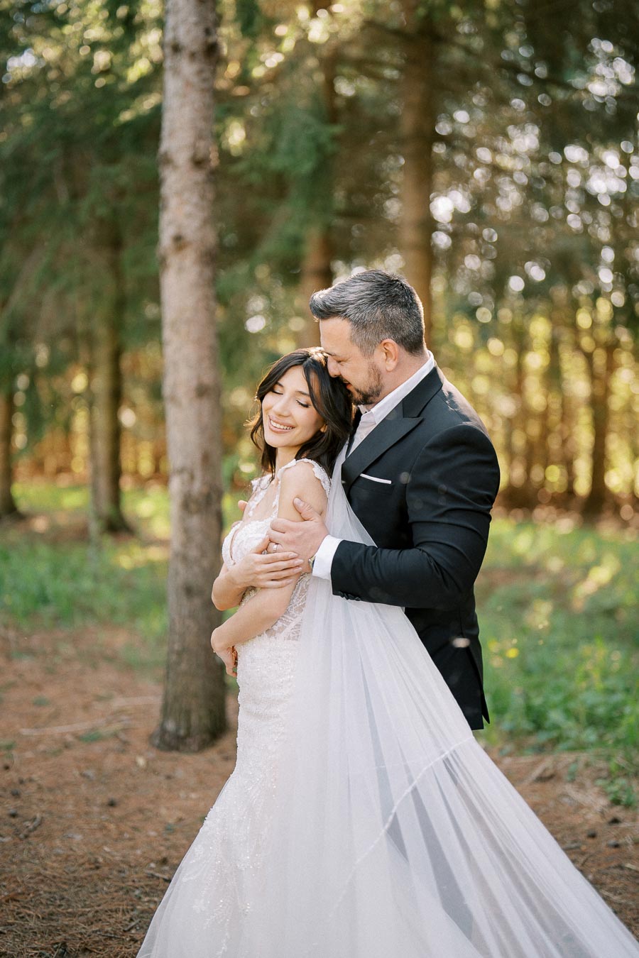 A bride and groom embrace lovingly in a sunlit forest, showcasing a romantic outdoor wedding atmosphere.