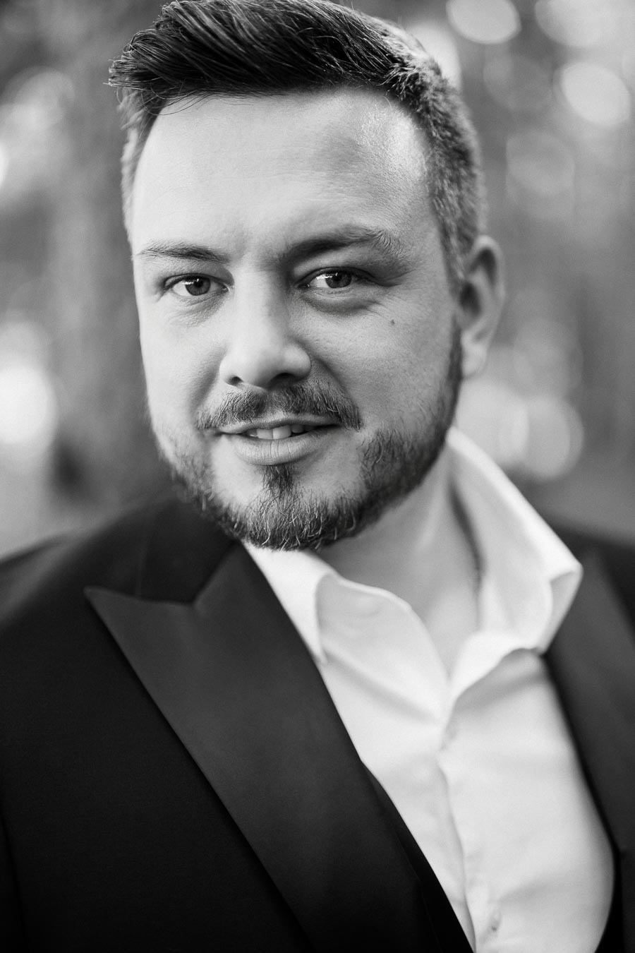 Black and white portrait of a man in a formal suit with a blurred outdoor background.