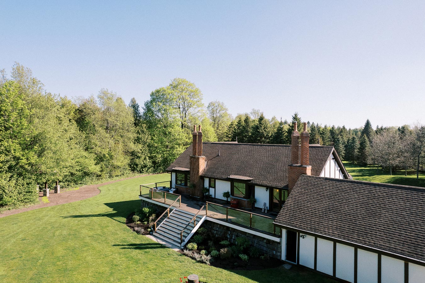 Serene countryside home surrounded by lush greenery and spacious lawn under a clear blue sky.