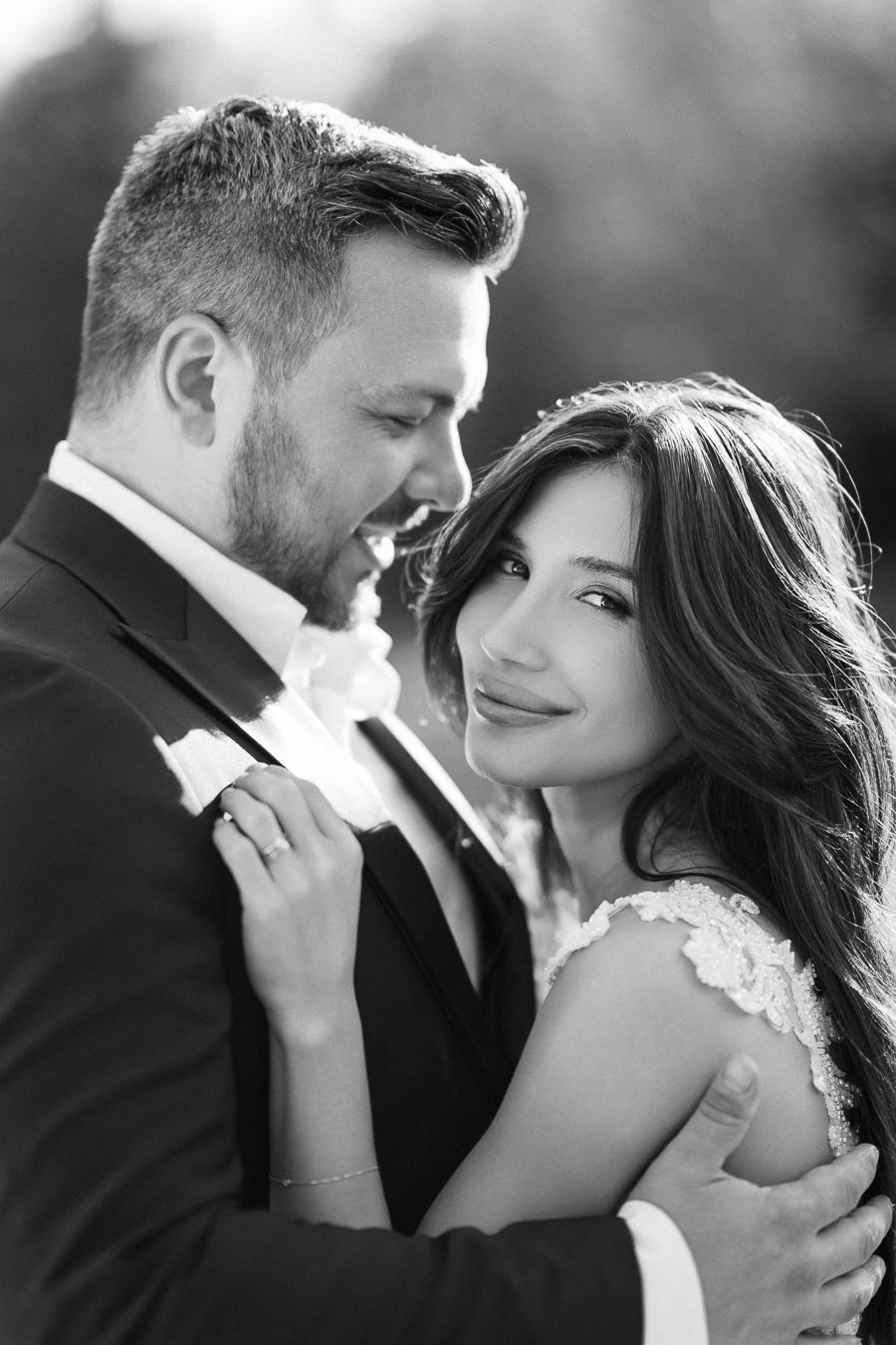 Romantic black and white photo of a couple embracing on their wedding day, showcasing the bride's elegant lace dress and the groom's formal suit.