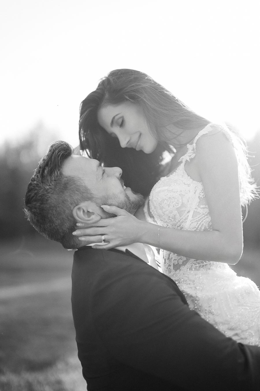 A romantic black and white photo of a groom lifting his bride in an embrace, capturing a tender moment on their wedding day.