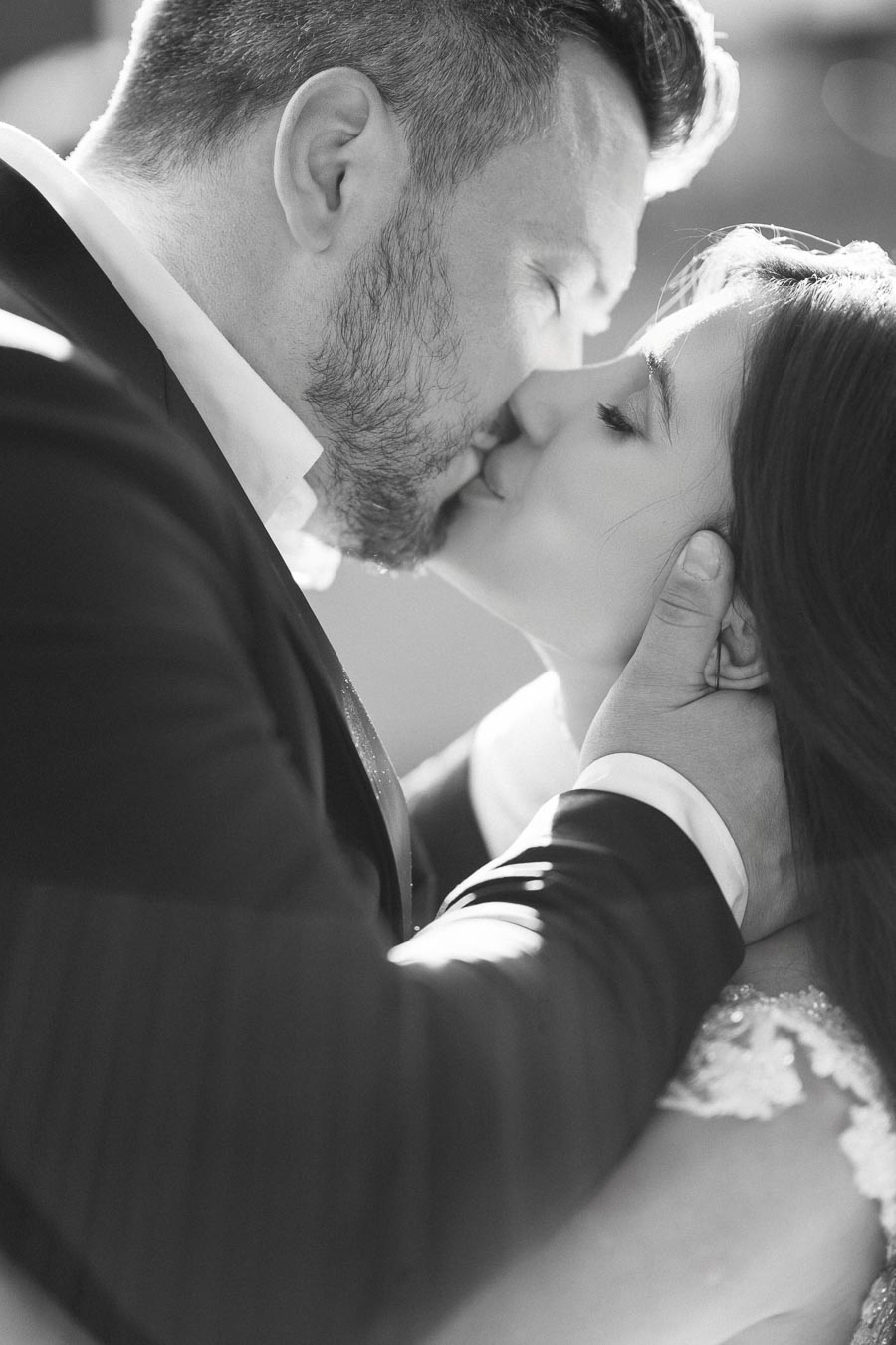 A black and white photograph of a couple sharing a romantic kiss, with the man gently holding the woman's face, capturing an intimate and tender moment.
