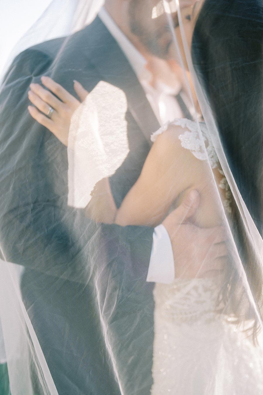 Romantic wedding moment with bride and groom embracing under a delicate veil, showcasing a tender and intimate connection.