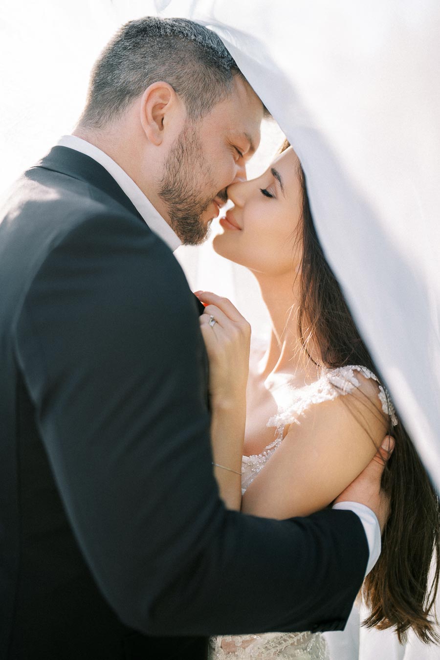 A romantic wedding moment with a bride and groom embracing under a white veil, capturing intimate love and joy on their special day.