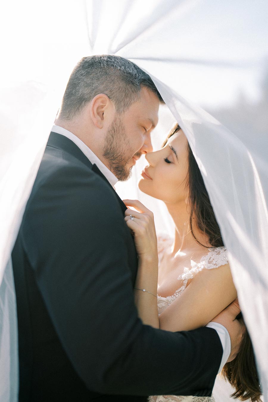 Romantic wedding photo featuring a bride and groom sharing an intimate moment under a delicate veil, capturing love and tenderness on their special day.