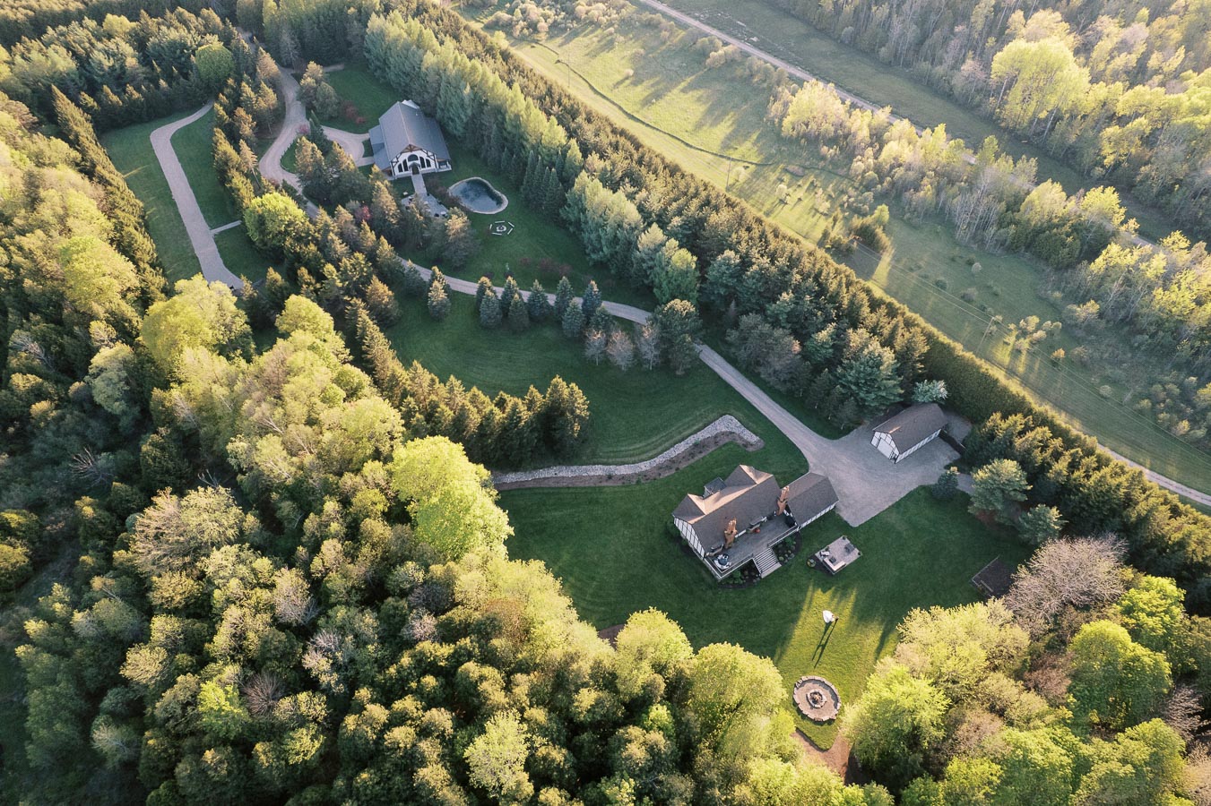 Arial view of an expansive countryside estate featuring lush green landscapes, well-maintained gardens, winding pathways, and several residential buildings nestled amongst dense forests.